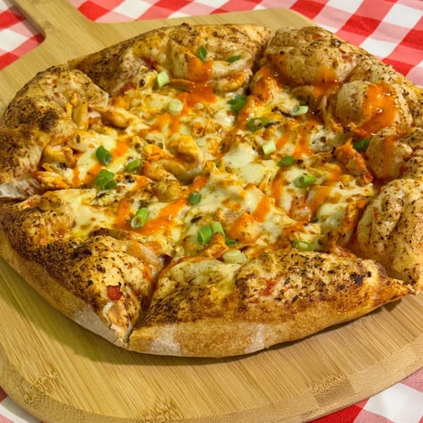 Fryer's Roadside buffalo chicken pizza with melted cheese, hot sauce, and green onions on a wooden board.