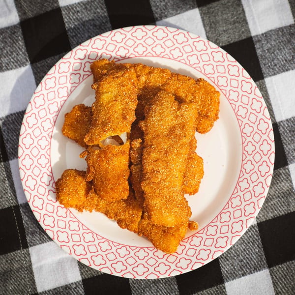 A plate of golden-brown fried chicken tenders, seasoned with spices, sits on a black and white checkered tablecloth.