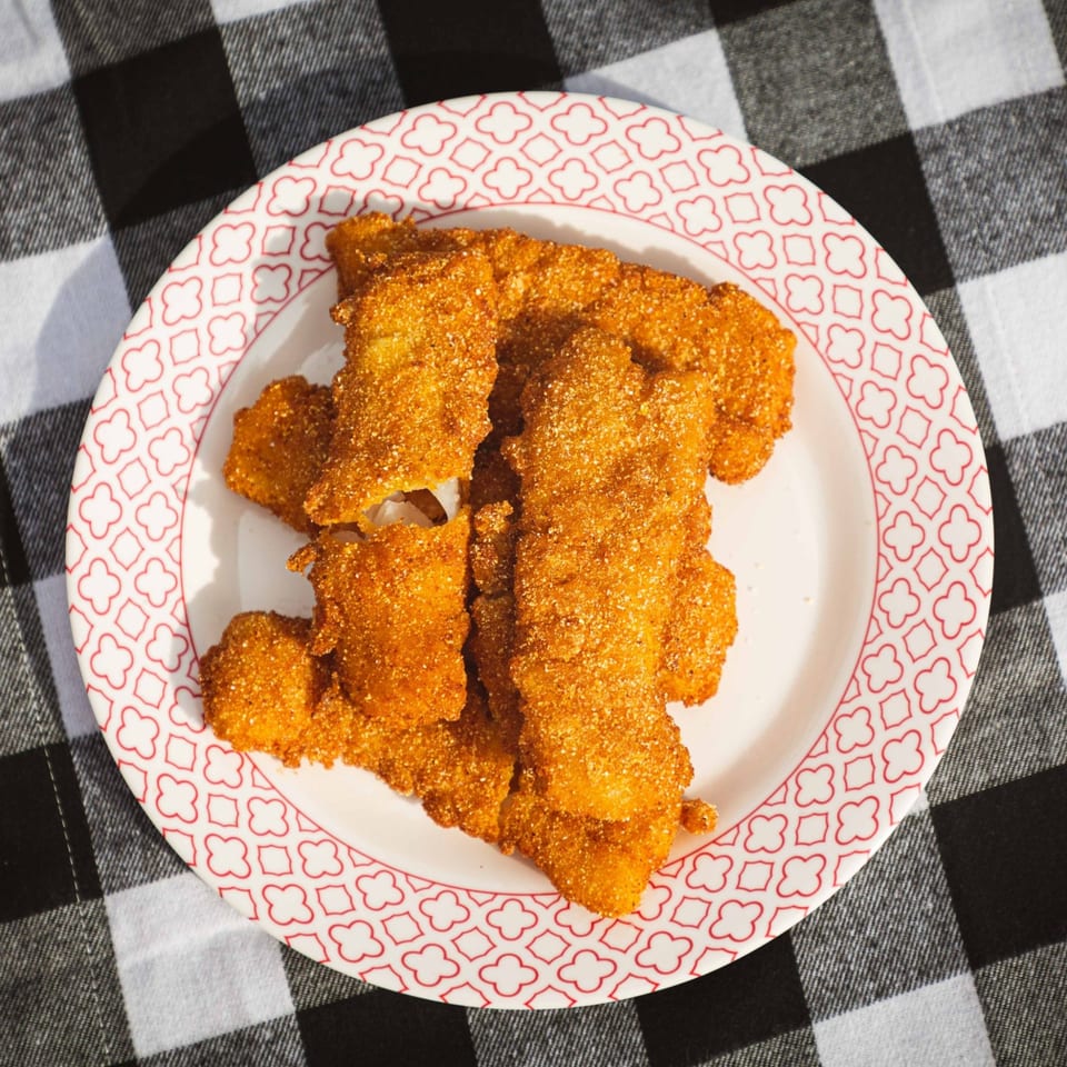 A plate of golden-brown fried chicken tenders, seasoned with spices, sits on a black and white checkered tablecloth.