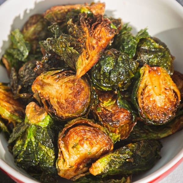 Close-up of crispy, roasted Brussels sprouts with golden-brown edges in a white bowl.
