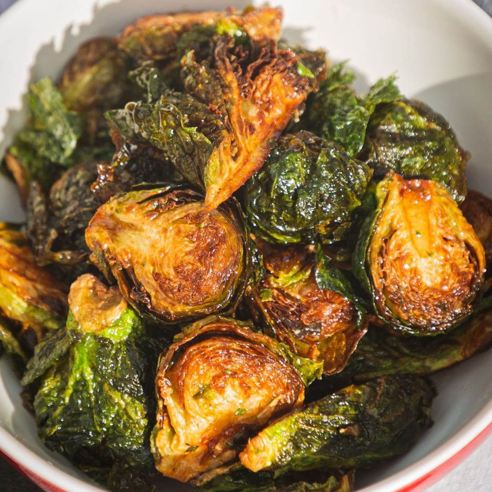 Close-up of crispy, roasted Brussels sprouts with golden-brown edges in a white bowl.